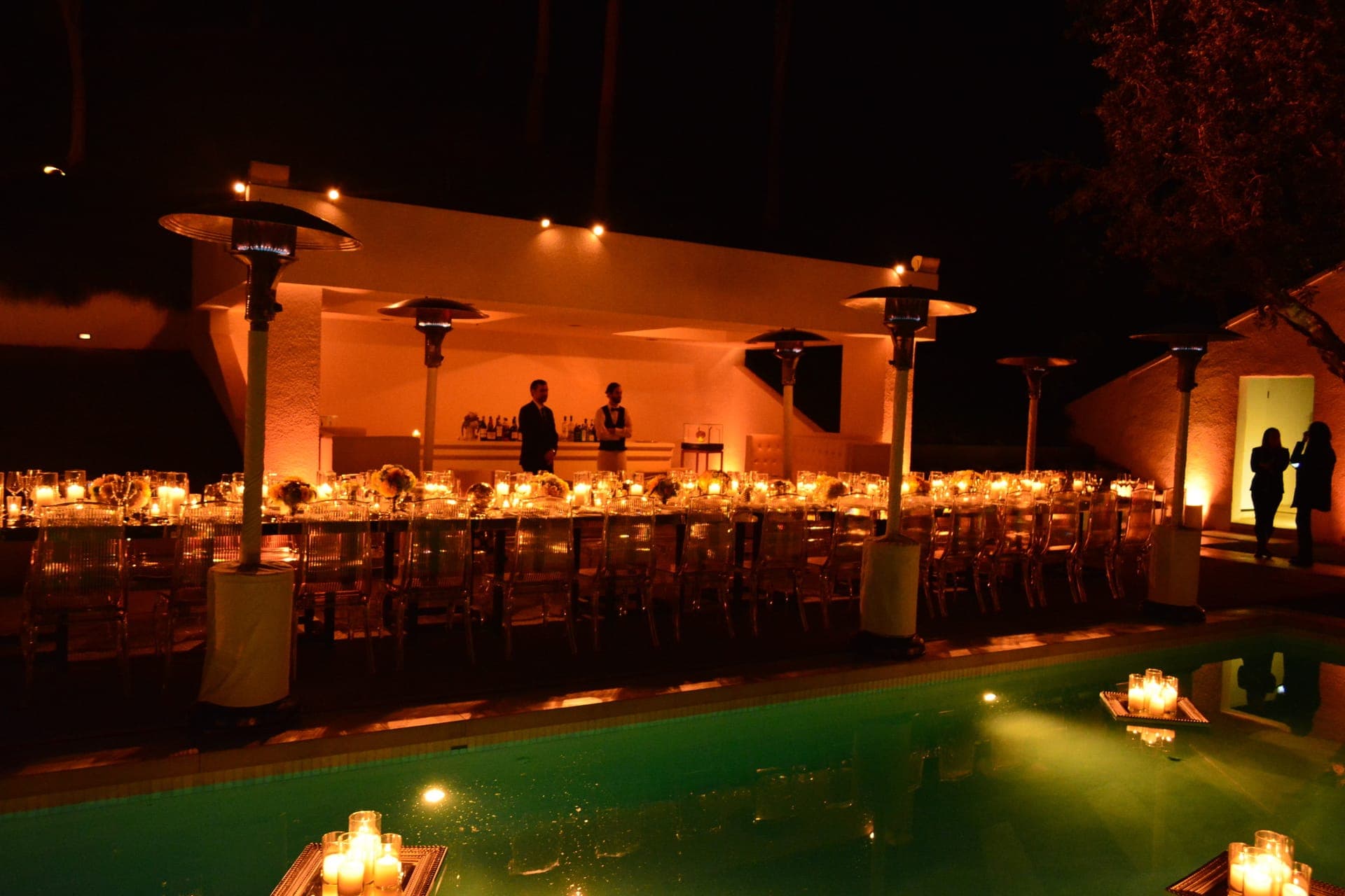 Long poolside dinner tables glowing in candlelight